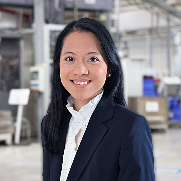 Trang Grün im Buisness Outfit vor einer Produktionsmaschine