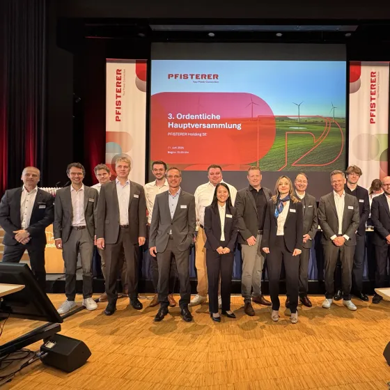 Gruppenfotos von etwa 15 Personen auf einer Bühne bei der 3. Ordentlichen Hauptversammlung der PFISTERER Holding SE am 11. Juni 2026. Im Hintergrund eine Präsentationsleinwand mit dem PFISTERER-Logo und dem Tagungstitel sowie zwei Roll-up-Banner mit der Firmenmarke. Die Teilnehmenden sind in Business-Kleidung gekleidet und stehen nebeneinander für das offizielle Gruppenfoto.